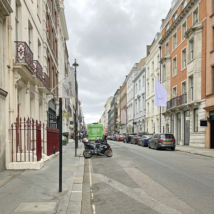 Looking up Albemarle Street, Mayfair: Georgian stone and red brick buildings with ironwork balconies and flags on both sides, cars parked along the street.